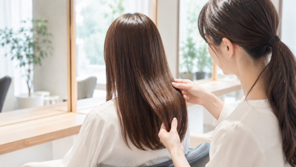 明るいサロンで美容師が女性のツヤのある髪を後ろからチェックする様子