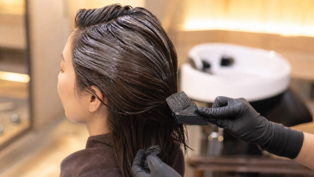 サロンでヘアカラー剤を髪に塗布される30代女性、ケミカルダメージのイメージ