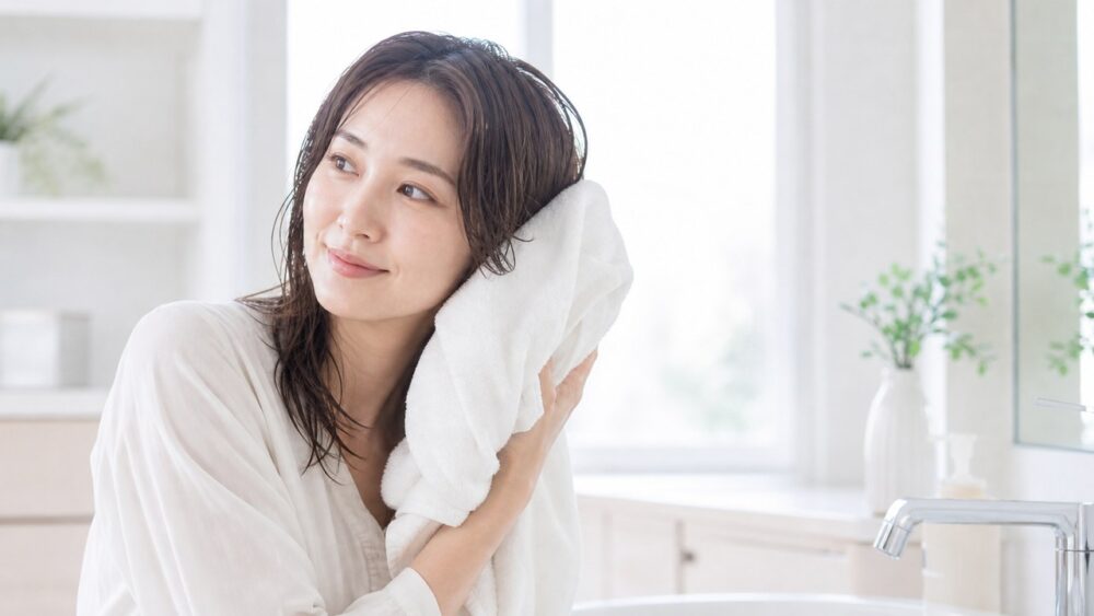 髪をタオルで優しく押さえながら拭く女性、優しい習慣のイメージ