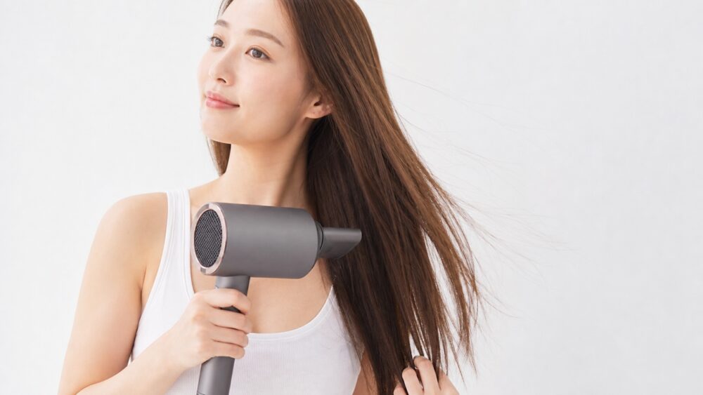 ドライヤーで根元から毛先へ髪を乾かす女性