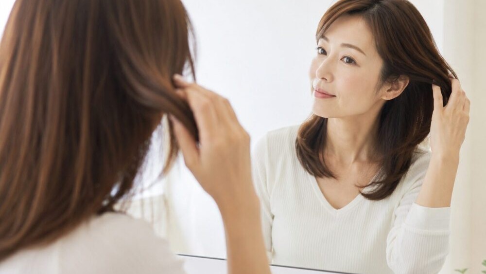 ヘアゴムを外して鏡で髪の結び跡を確認している女性