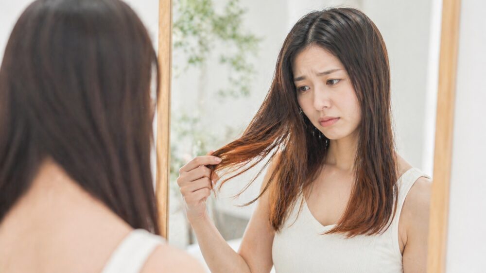 鏡を見て髪のカラー褪色に悩む日本人女性