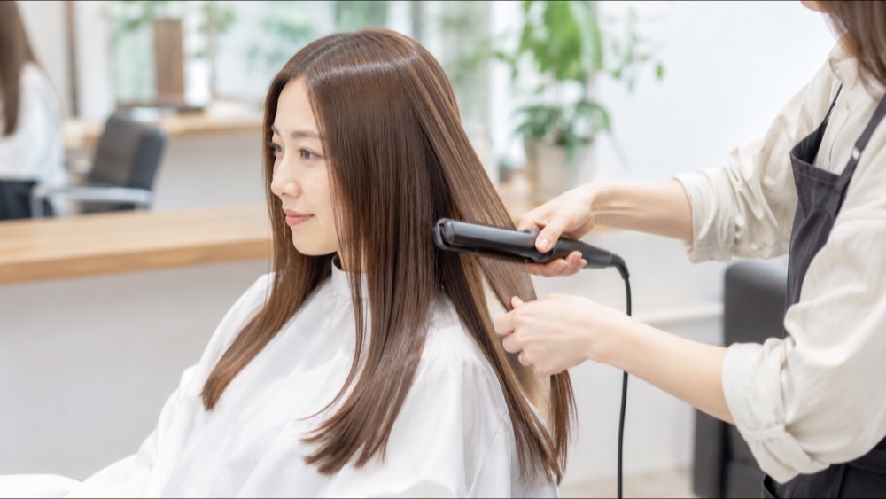 美容室で美容師がストレートアイロンで髪をまっすぐに伸ばす施術シーン