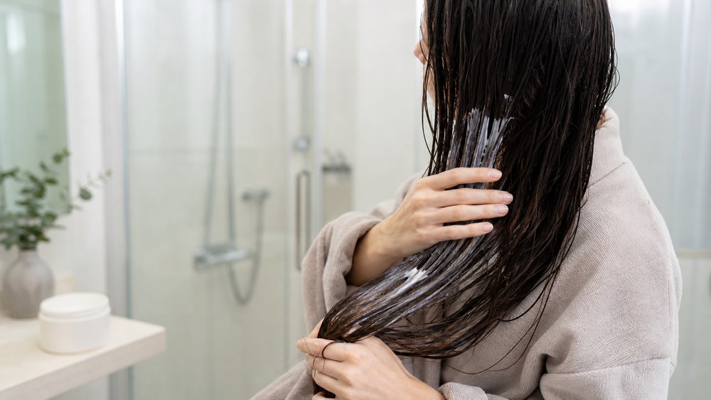 濡れた髪の中間から毛先にトリートメントをなじませる女性
