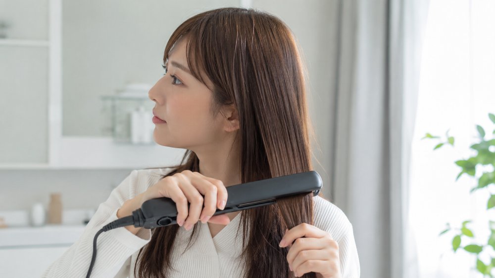 茶色いカラーヘアをはさむヘアアイロンと立ちのぼる湯気の接写