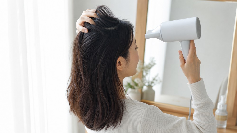 髪の根元をドライヤーで乾かす女性
