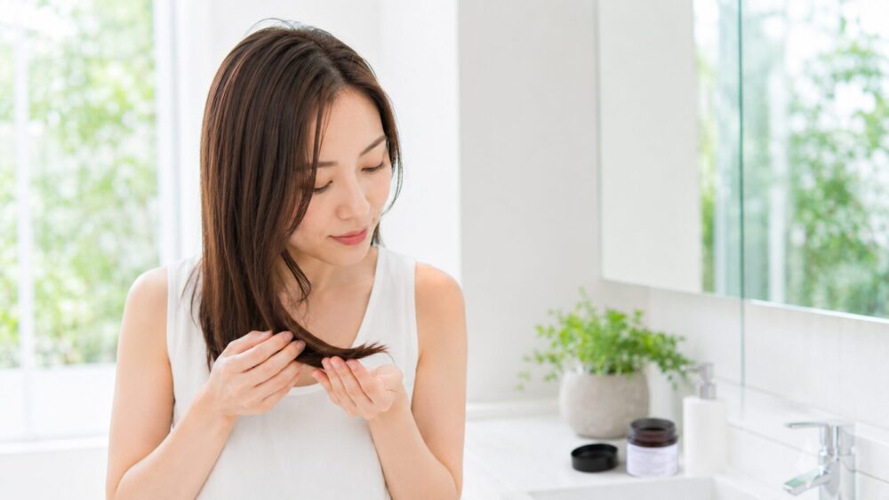 洗面台でヘアバームを髪になじませる日本人女性