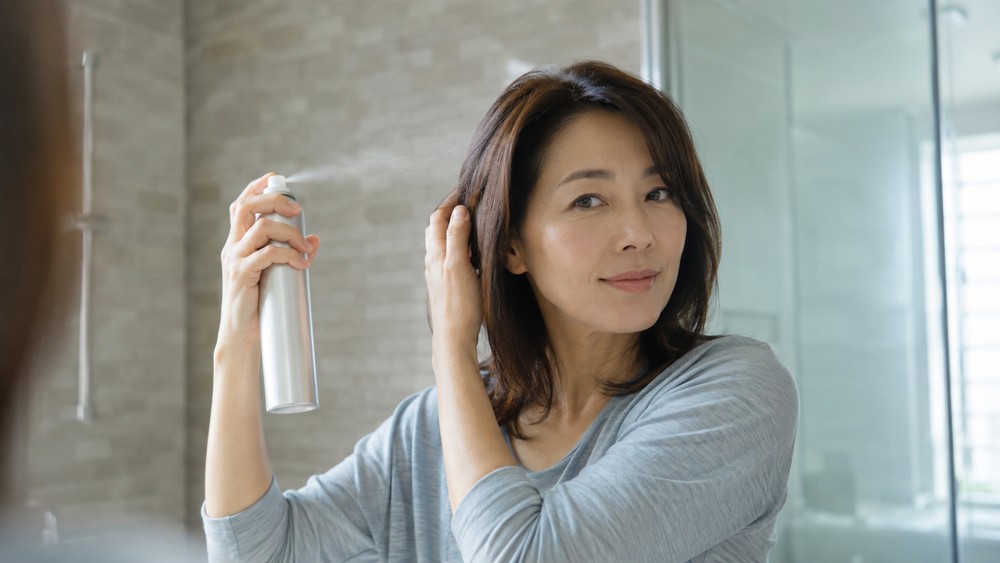 ハードスプレーで髪の表面を整える女性