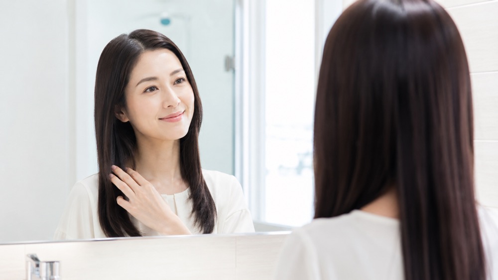 ツヤのあるストレートヘアで鏡を見て微笑む女性