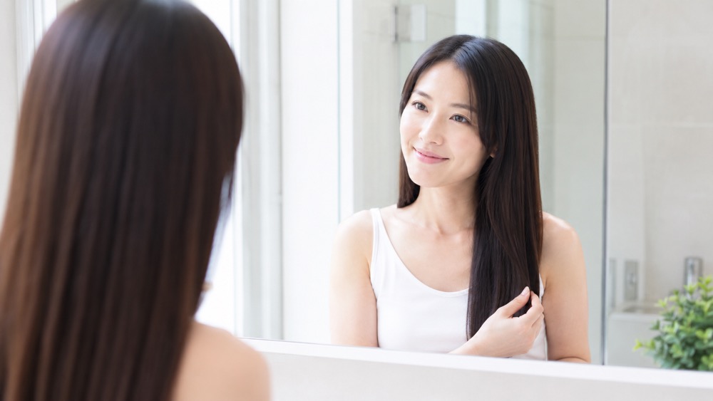 縮毛矯正でキレイに伸びたストレートヘアを鏡で確認する女性