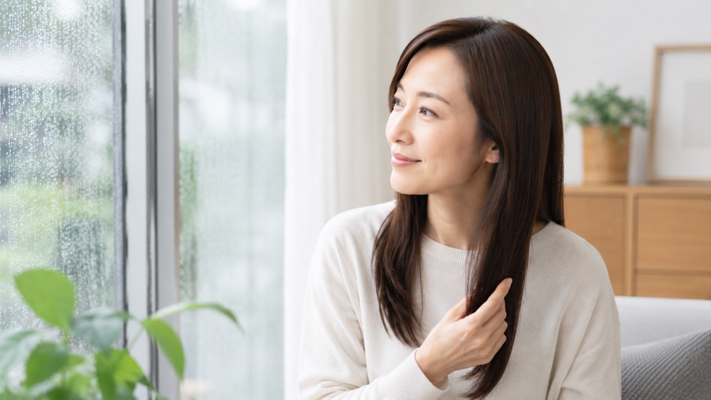梅雨の窓辺でまとまった髪を整える女性