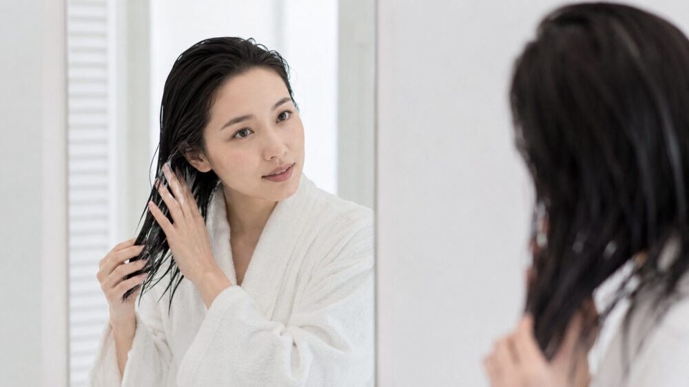 鏡の前で濡れた髪にトリートメントを塗る日本人女性