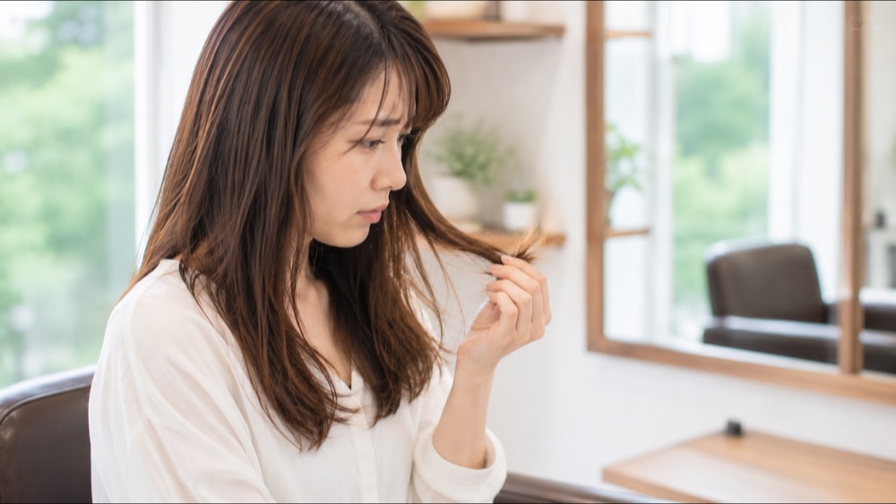 傷んで広がった毛先を指で確かめる女性