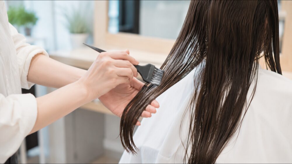 縮毛矯正の薬剤を髪の中間から毛先へ塗布する美容師の手元