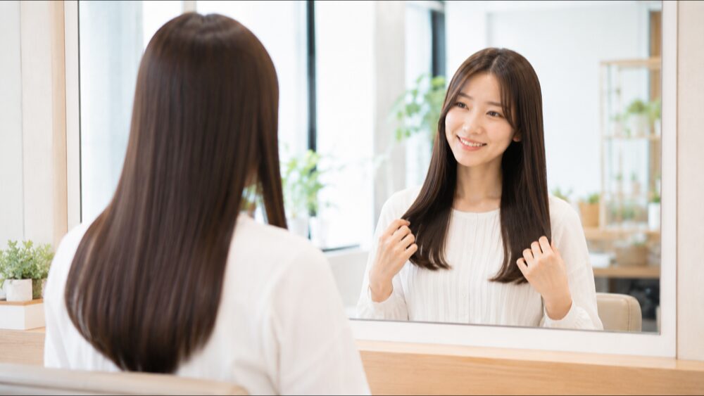 ツヤのあるまっすぐな髪を鏡で見て喜ぶ若い女性