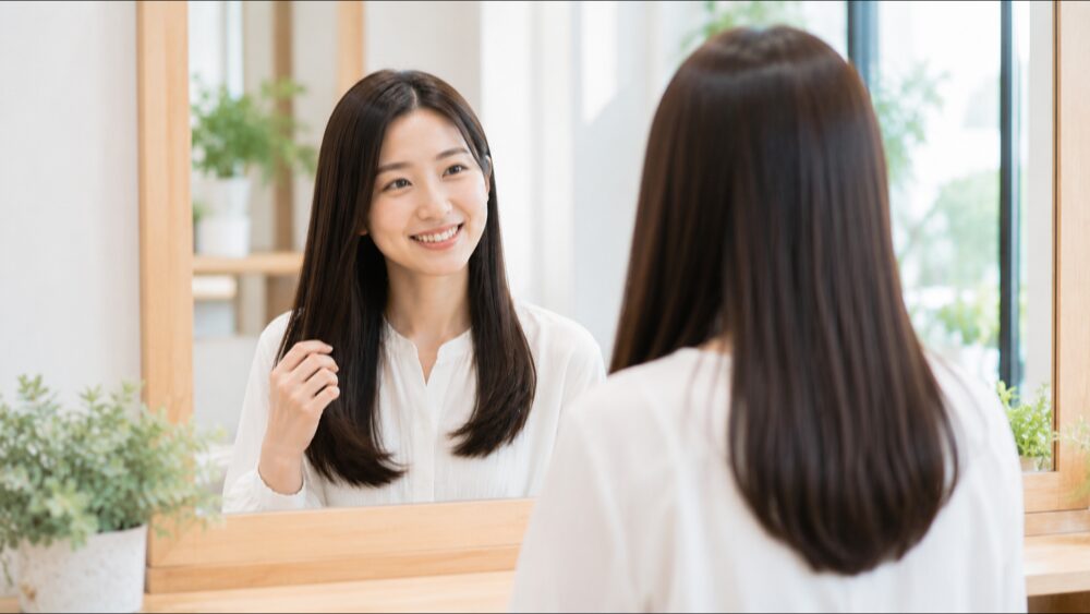 施術後に鏡の前でツヤのあるストレートヘアを見て微笑む女性