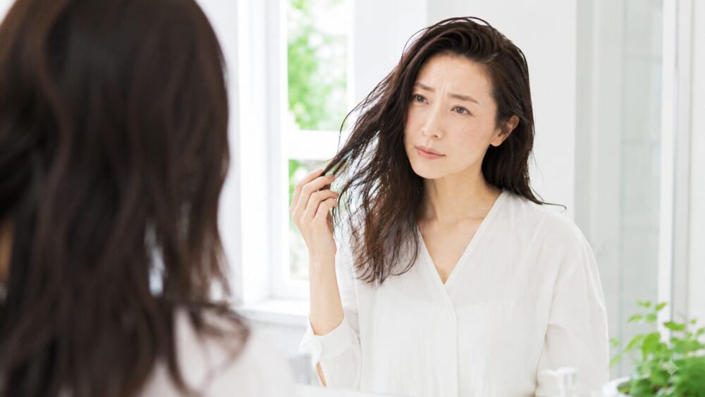 鏡の前で髪のうねりを気にする日本人女性