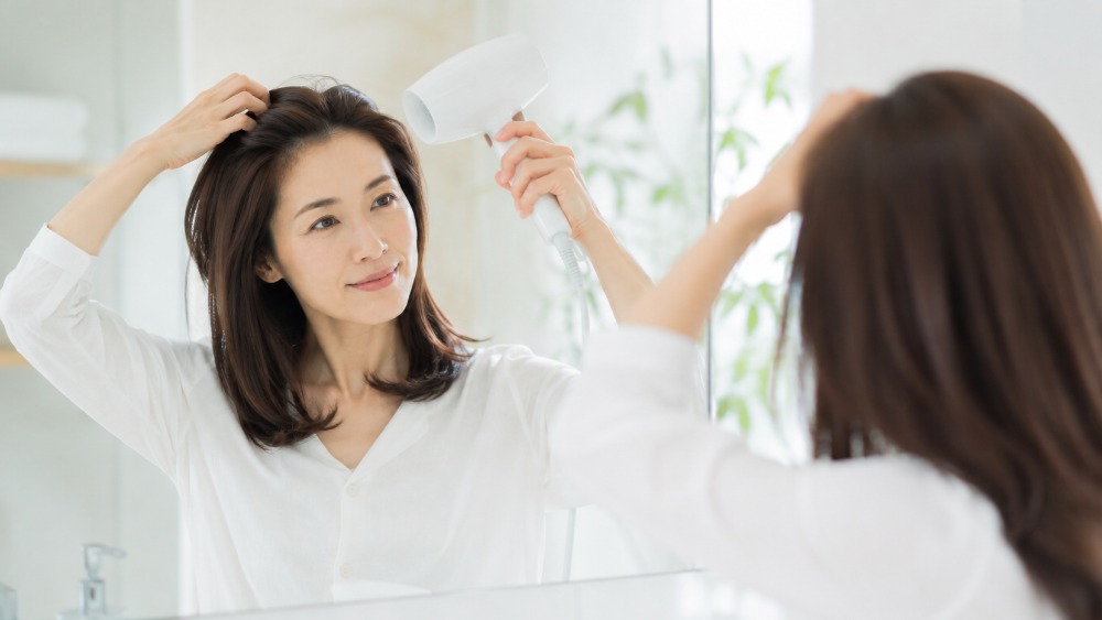 鏡の前で根元を持ち上げながらドライヤーの風を根元に当てる女性