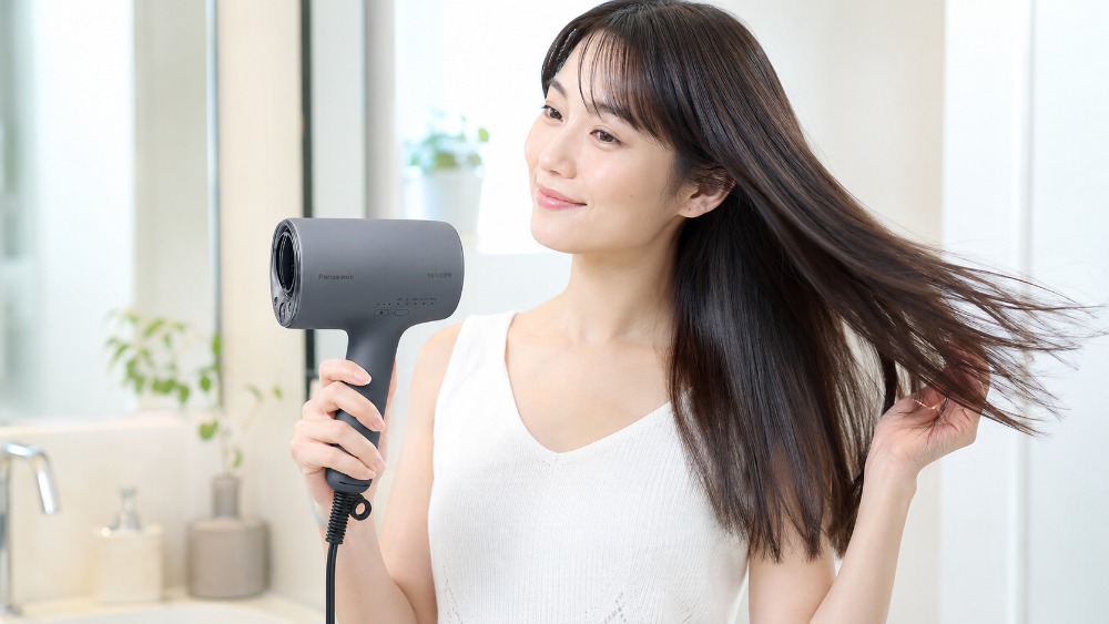 明るい洗面所でドライヤーを手にツヤのあるまとまった髪に風を当てる女性