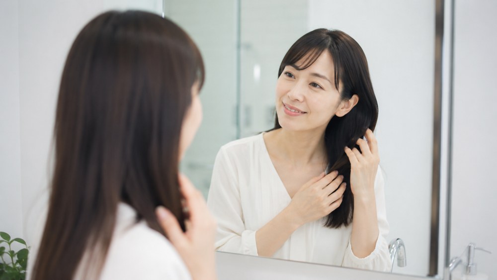 鏡の前でサラサラの髪に触れる女性