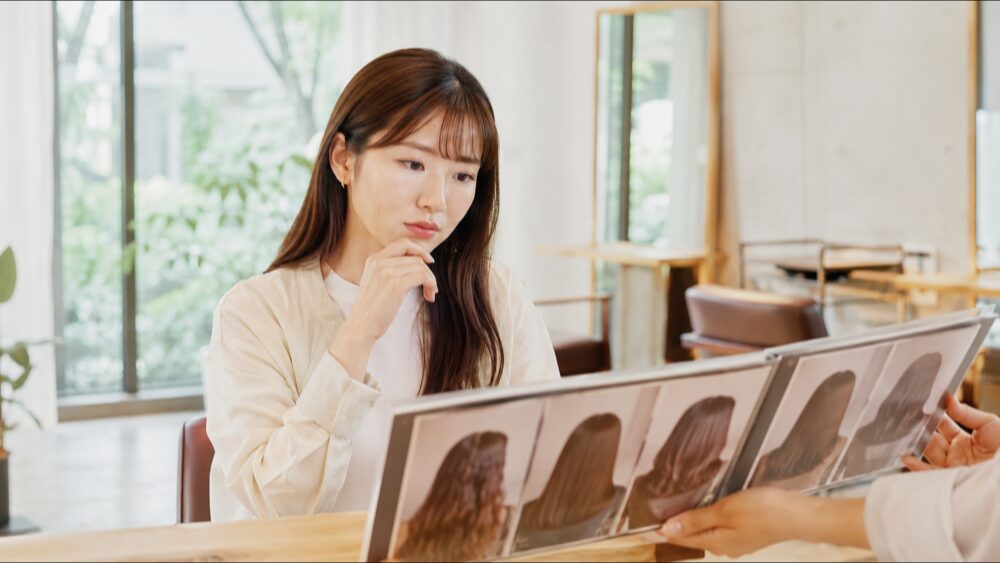 美容室でヘアスタイルの写真を見比べる日本人女性