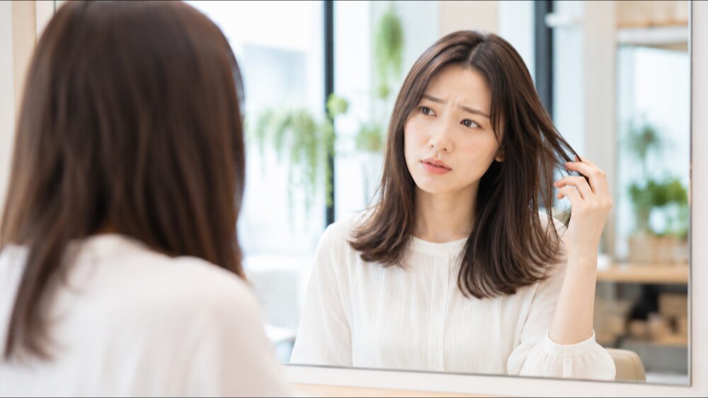 美容室で鏡を見ながら自分の髪を気にする日本人女性