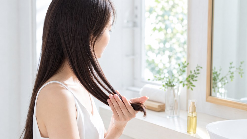 洗い流さないトリートメントオイルを毛先につける日本人女性