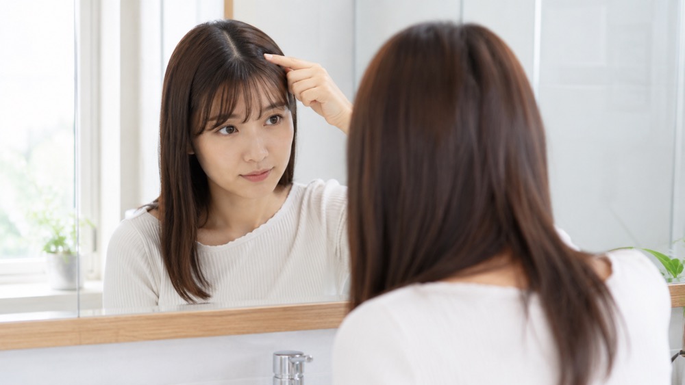 伸びてきた根本のクセを鏡で確認している女性