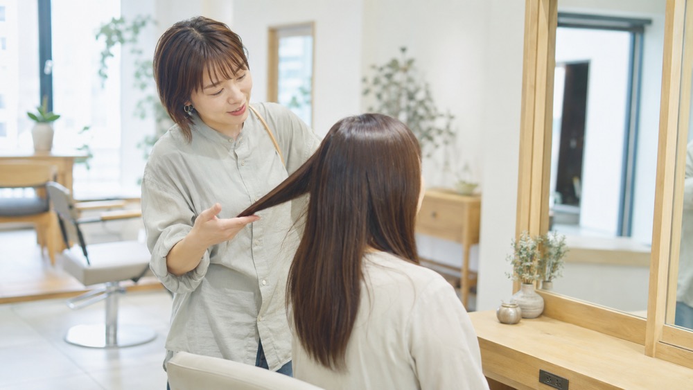 縮毛矯正の仕組みを美容師が鏡の前で説明する様子
