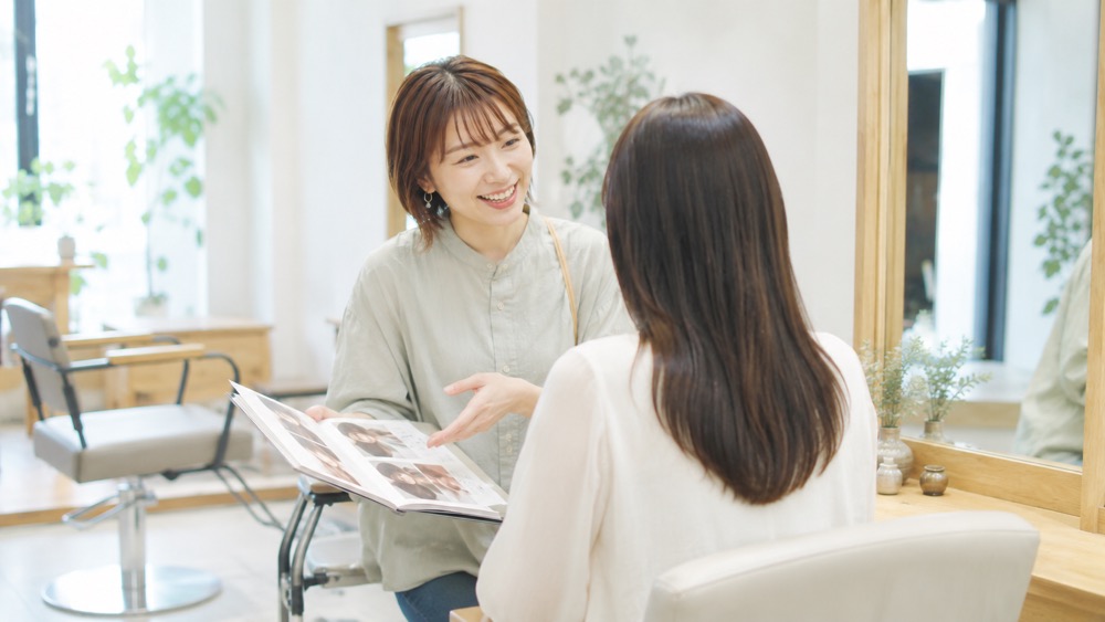 美容師とカタログを見て笑顔で相談する女性