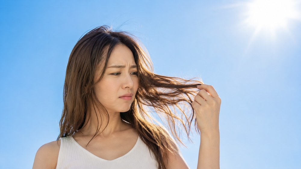 夏の日差しの下でパサついた髪を手に取り困った表情の日本人女性