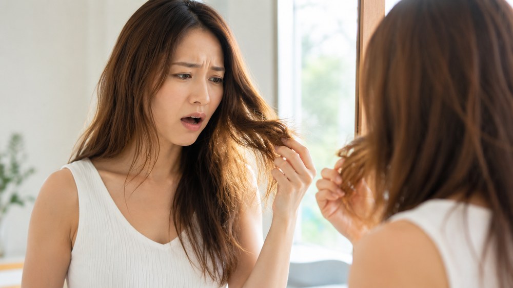 鏡の前で退色した毛先を手に取りショックを受ける日本人女性