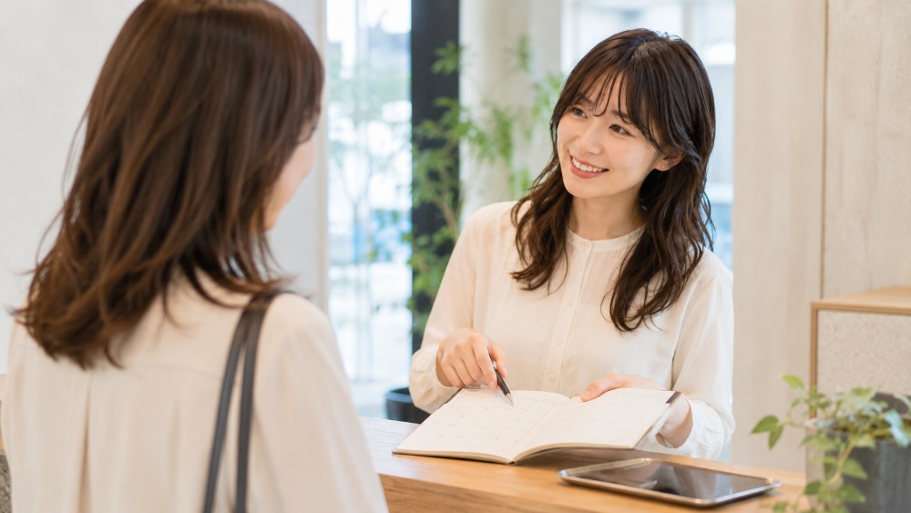 美容室の受付カウンターで次回の予約を相談する美容師と客