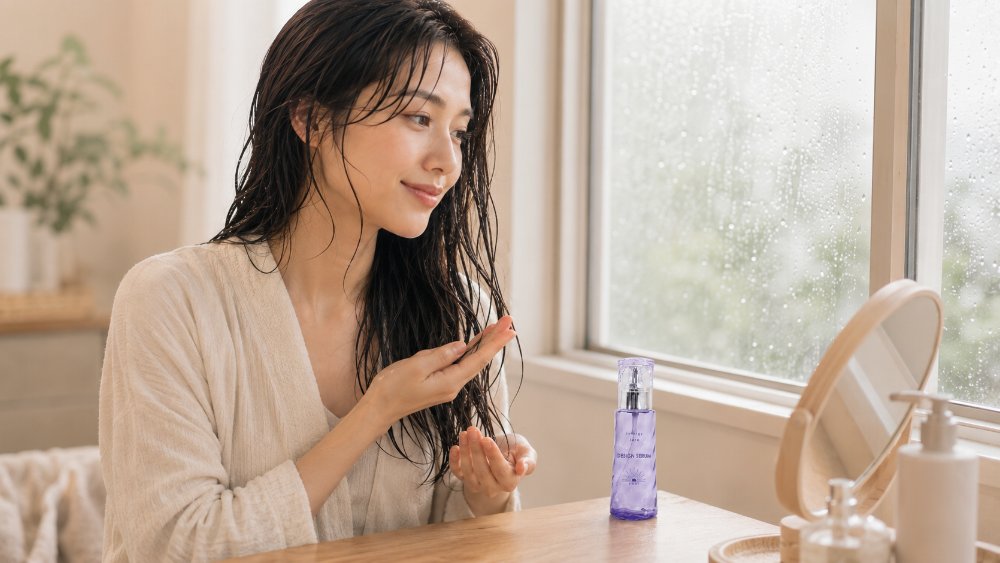 雨の日の窓辺で髪の中間から毛先にセラムをなじませる様子