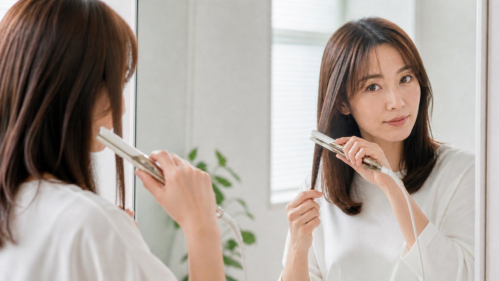 鏡の前で毛束を取りリファストレートアイロンCSでゆっくり伸ばす女性
