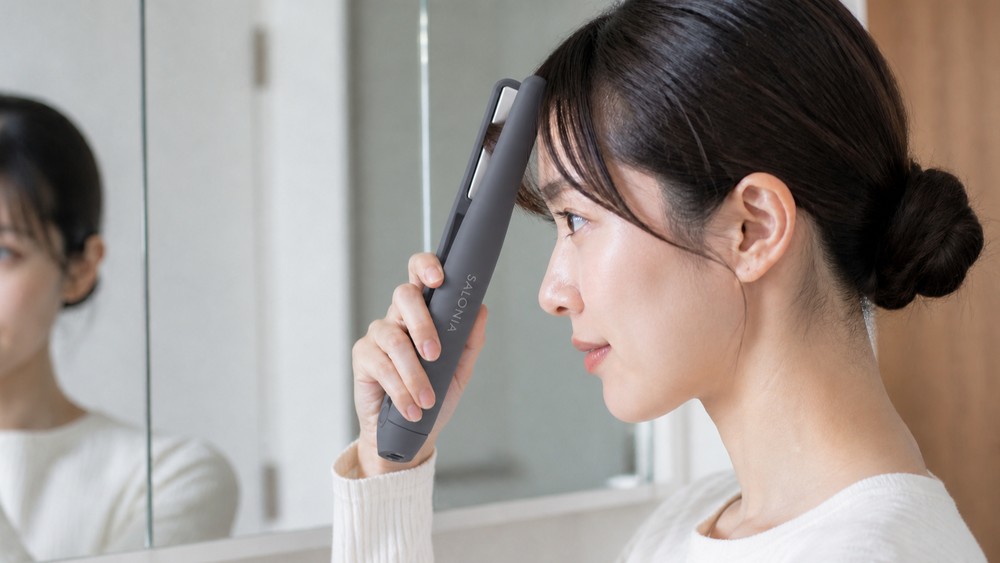 鏡の前でコードレスヘアアイロンを前髪に当てている女性