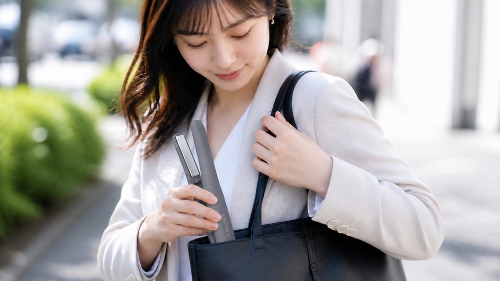 通勤バッグからコードレスヘアアイロンを取り出す女性