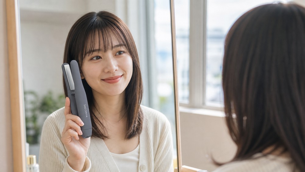 前髪を整え終えて鏡を見ながら微笑む女性とコードレスヘアアイロン