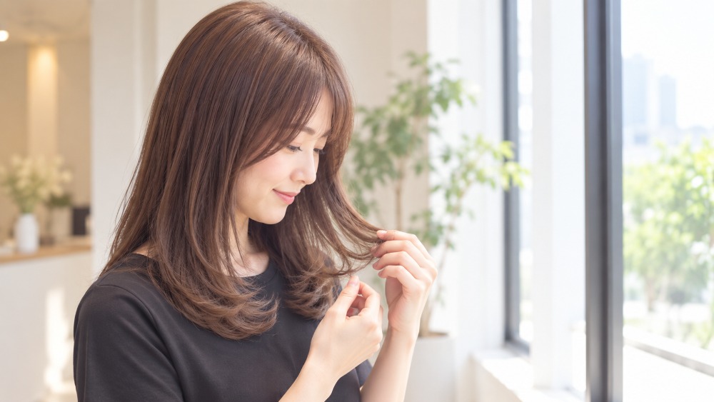 窓際で毛先のワンカールを確かめる女性