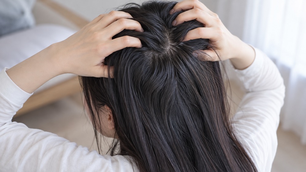 頭頂部の髪を分けて根元のうねりを確認する女性